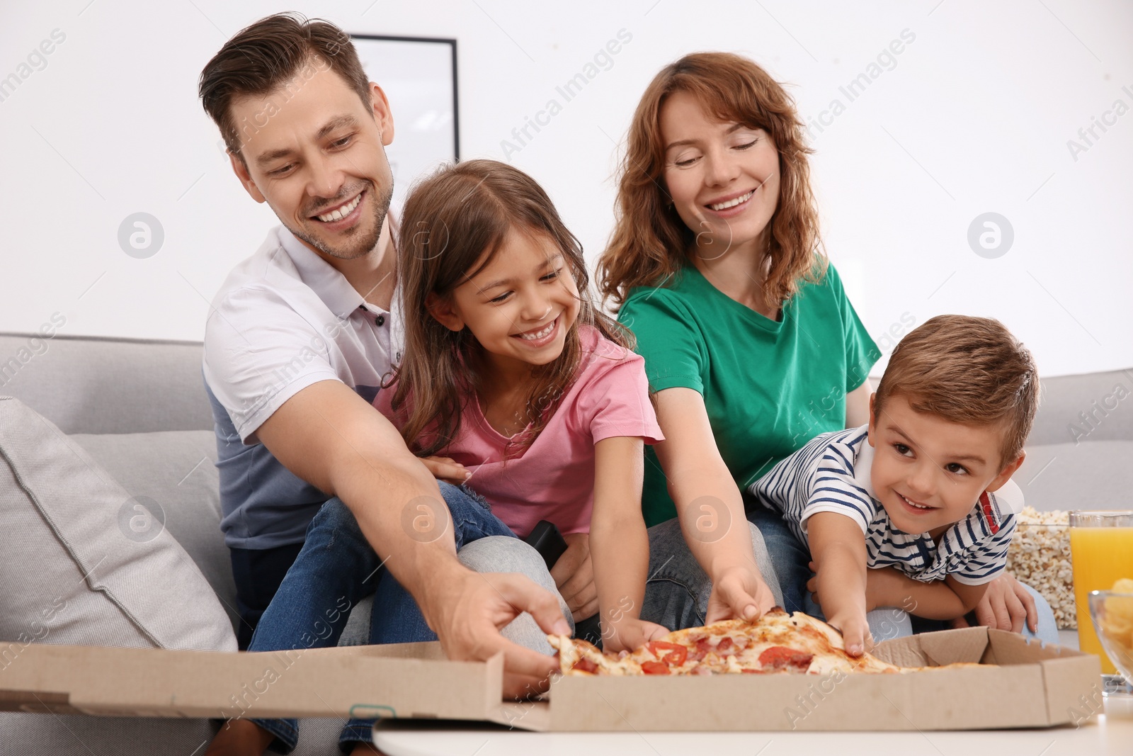 Photo of Family eating pizza while watching TV in room