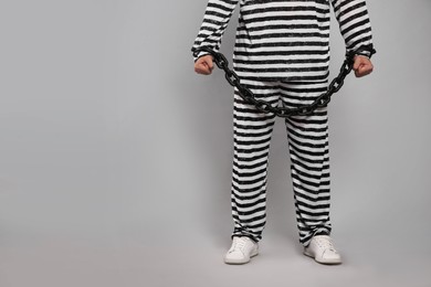 Photo of Prisoner in special uniform with chained hands on grey background, closeup. Space for text