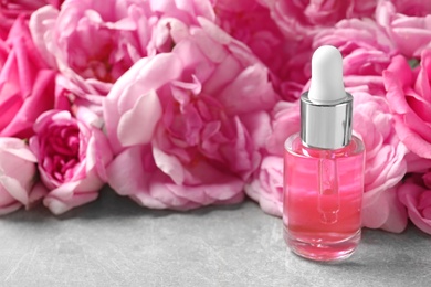 Photo of Bottle of rose essential oil and fresh flowers on table, space for text