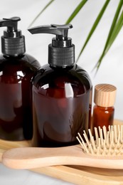 Photo of Shampoo bottles, wooden brush and essential oil on white table