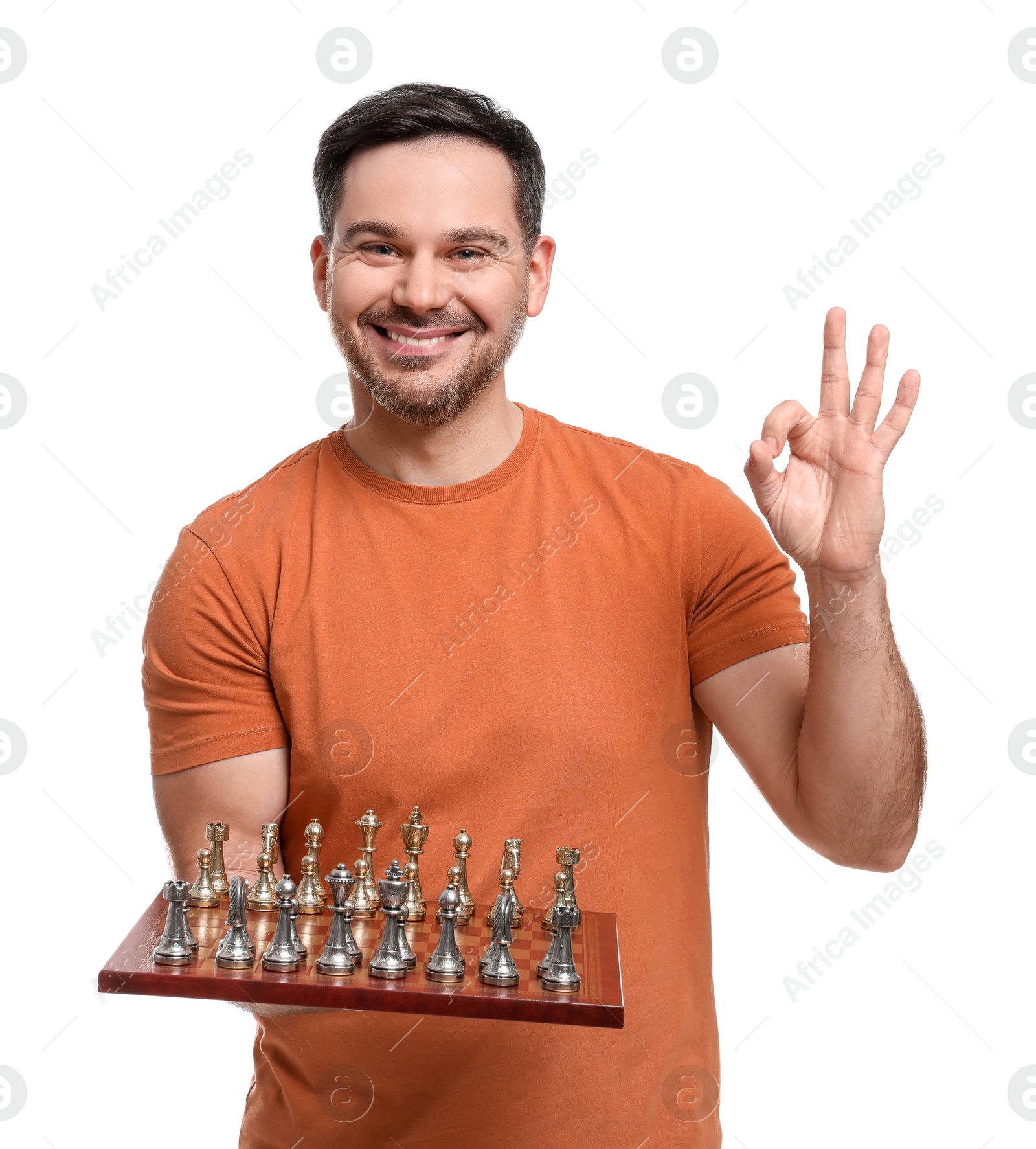 Photo of Smiling man holding chessboard with game pieces and showing OK gesture on white background