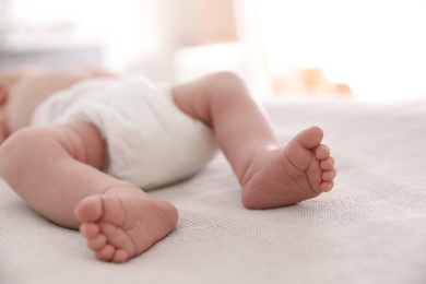 Photo of Cute little baby in diaper lying on bed in room, closeup