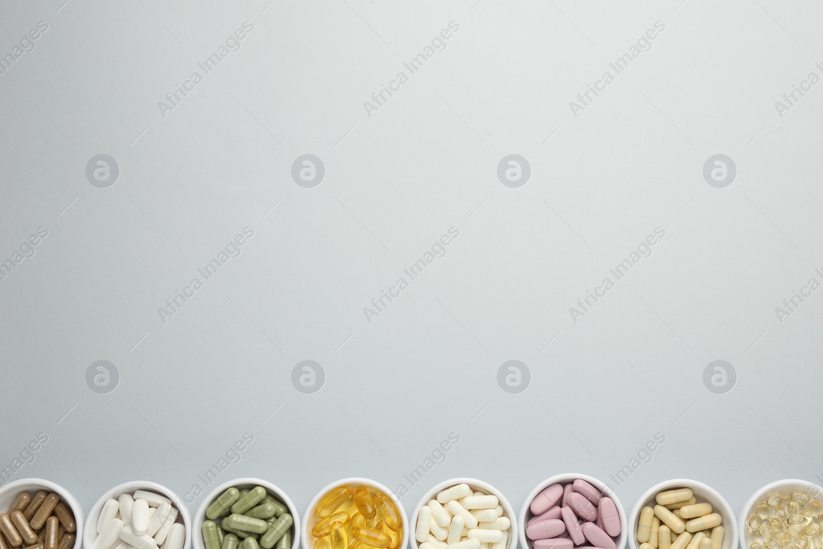 Photo of Different vitamin pills in bowls on grey background, flat lay. Space for text