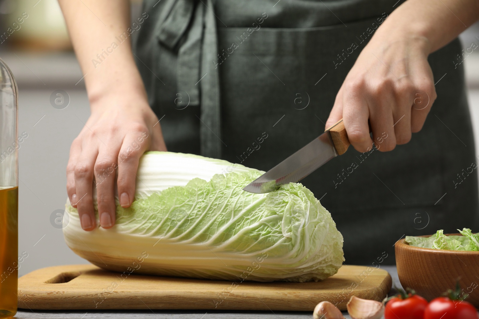 Photo of Woman cutting fresh chinese cabbage at grey wooden table in kitchen, closeup