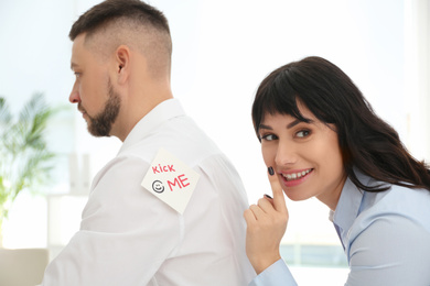 Young woman sticking KICK ME note to colleague's back in office. April fool's day