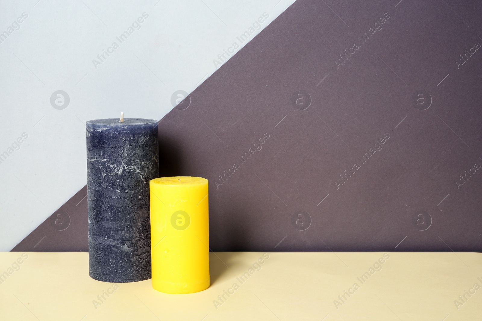 Photo of Decorative wax candles on table against color background