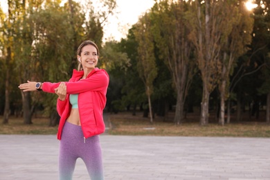 Photo of Young woman with wireless headphones listening to music while exercising outdoors. Space for text