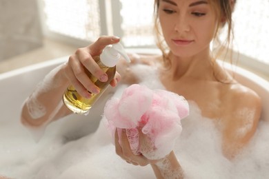 Photo of Beautiful woman pouring shower gel onto mesh pouf in bath indoors, focus on hands