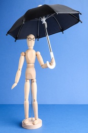 Photo of Wooden human figure with umbrella against light blue background