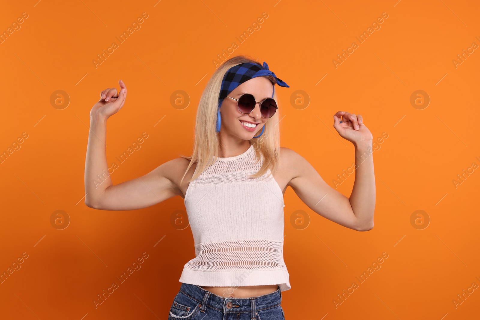 Photo of Portrait of smiling hippie woman in sunglasses on orange background