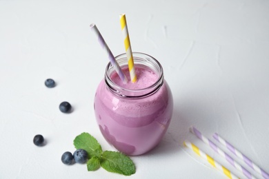 Jar of tasty milk shake and blueberries on light background