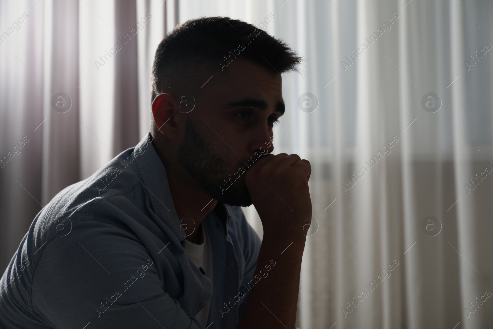 Photo of Sad man near window indoors. Space for text