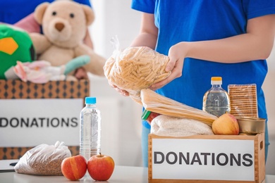 Photo of Female volunteer putting food products in donation box indoors