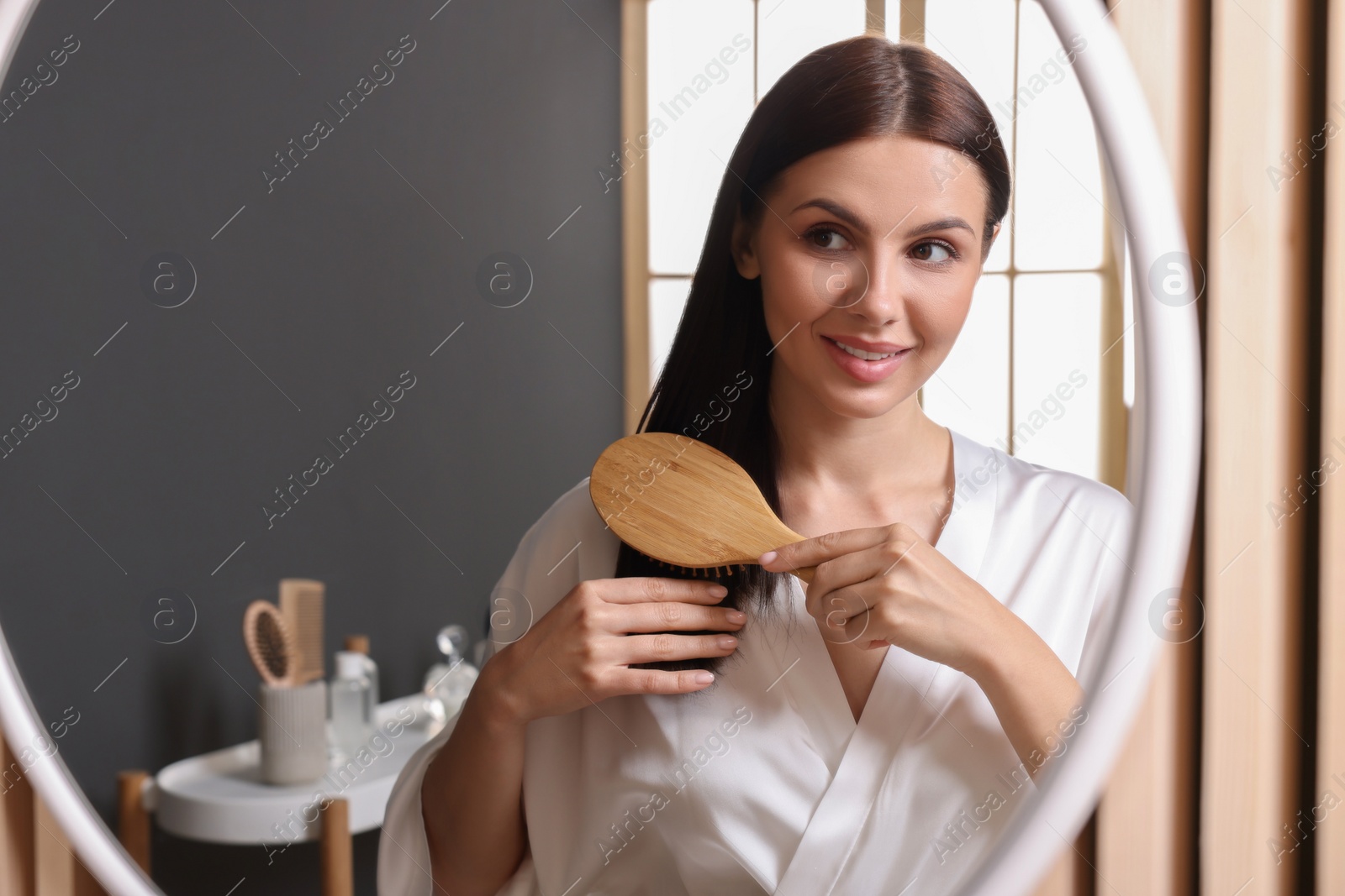 Photo of Beautiful woman brushing her hair near mirror in room