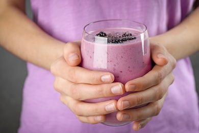Photo of Young woman holding glass of tasty blackberry smoothie, closeup