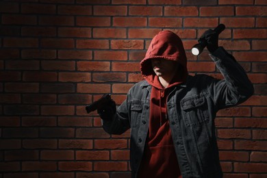 Thief in hoodie with gun and flashlight against red brick wall