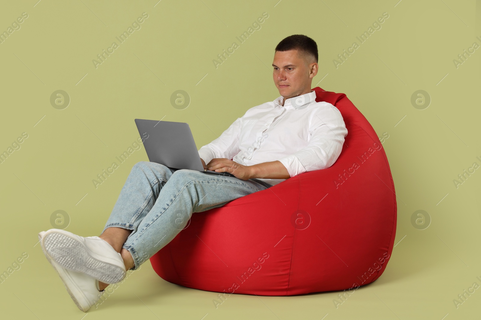 Photo of Handsome man with laptop on red bean bag chair against green background