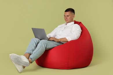 Photo of Handsome man with laptop on red bean bag chair against green background