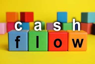 Image of Phrase Cash Flow made with letters and colorful cubes on yellow background