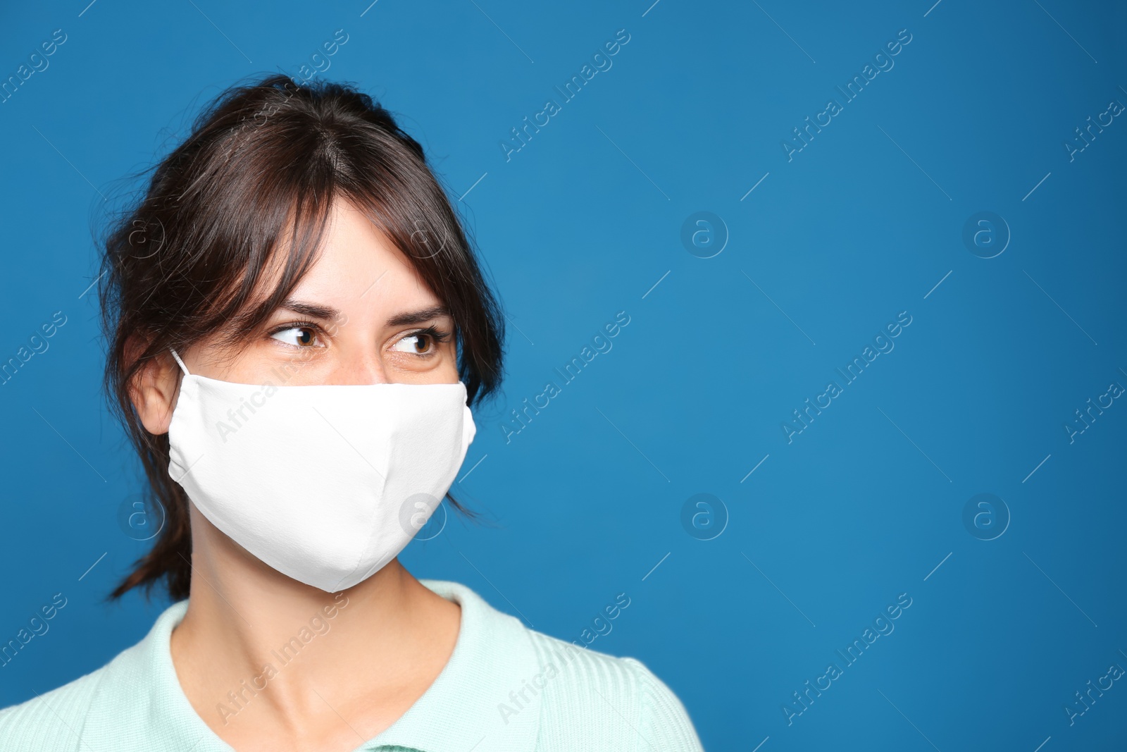 Photo of Young woman in protective face mask on blue background, space for text