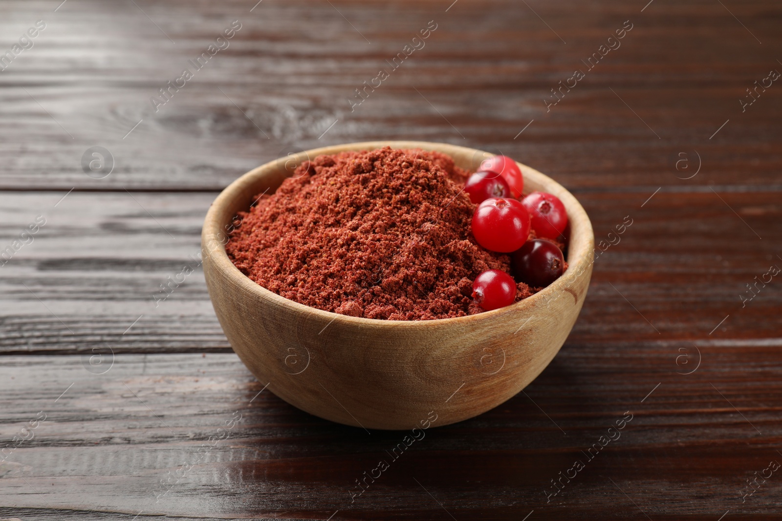 Photo of Dried cranberry powder and fresh berries in bowl on wooden table, closeup