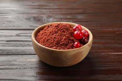 Photo of Dried cranberry powder and fresh berries in bowl on wooden table, closeup