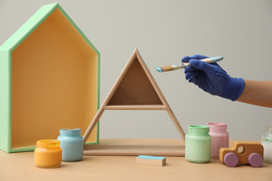 Photo of Decorator painting pyramid shaped shelf with brush at wooden table, closeup. Interior element