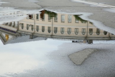 Reflection of beautiful building in puddle on asphalt