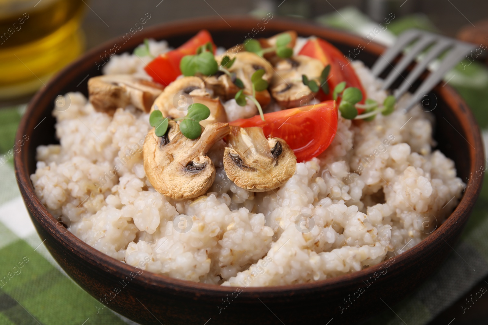 Photo of Delicious barley porridge with mushrooms, tomatoes and microgreens in bowl on table, closeup