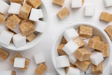 Photo of Different sugar cubes in bowls on white table, flat lay