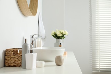 Vase with beautiful white roses and toiletries near sink in bathroom