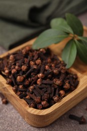 Wooden tray with aromatic cloves and green leaves on table, closeup