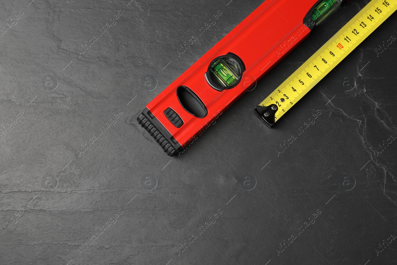 Photo of Building level and tape measure on black table, top view. Space for text