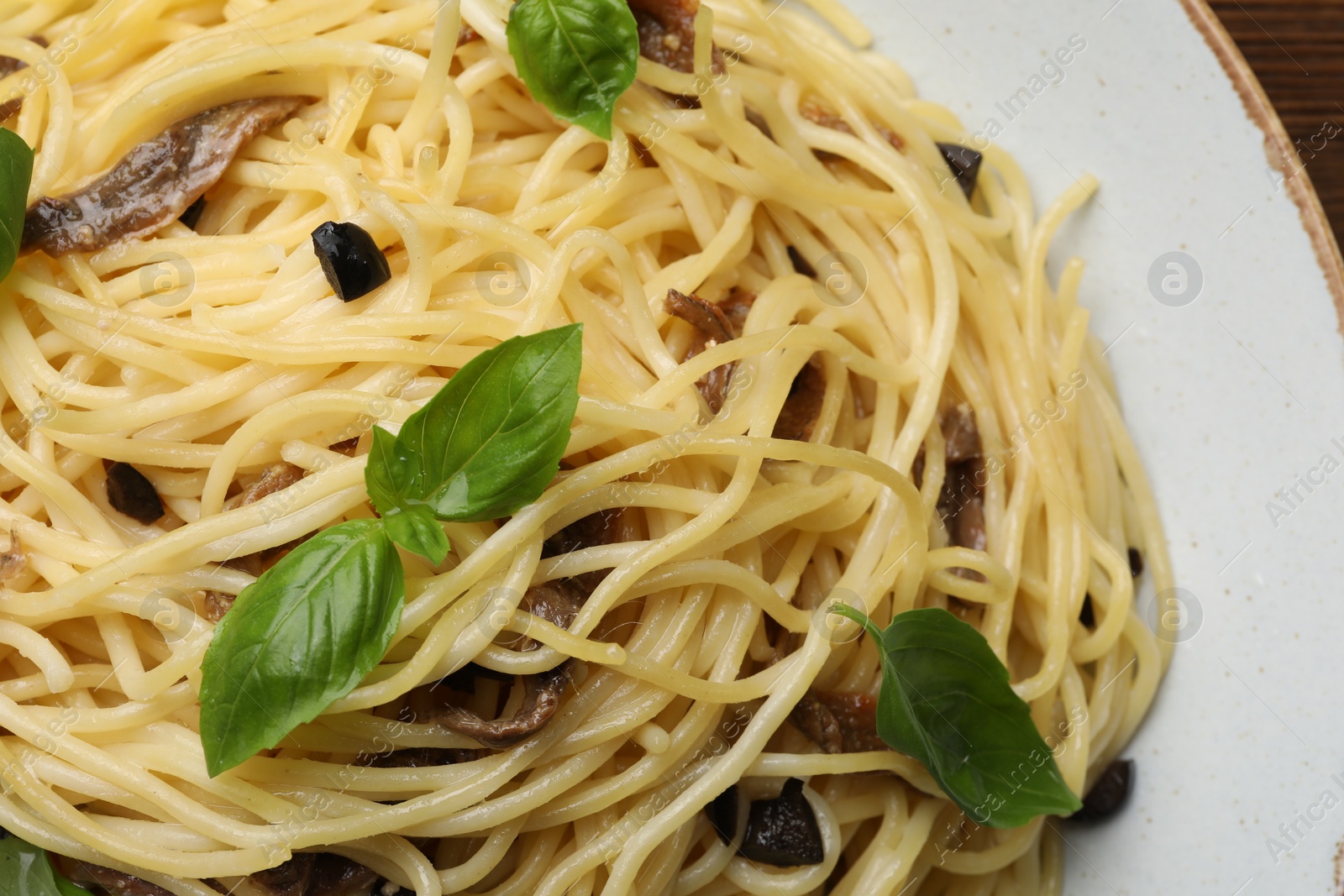 Photo of Delicious pasta with anchovies, olives and basil on plate, closeup