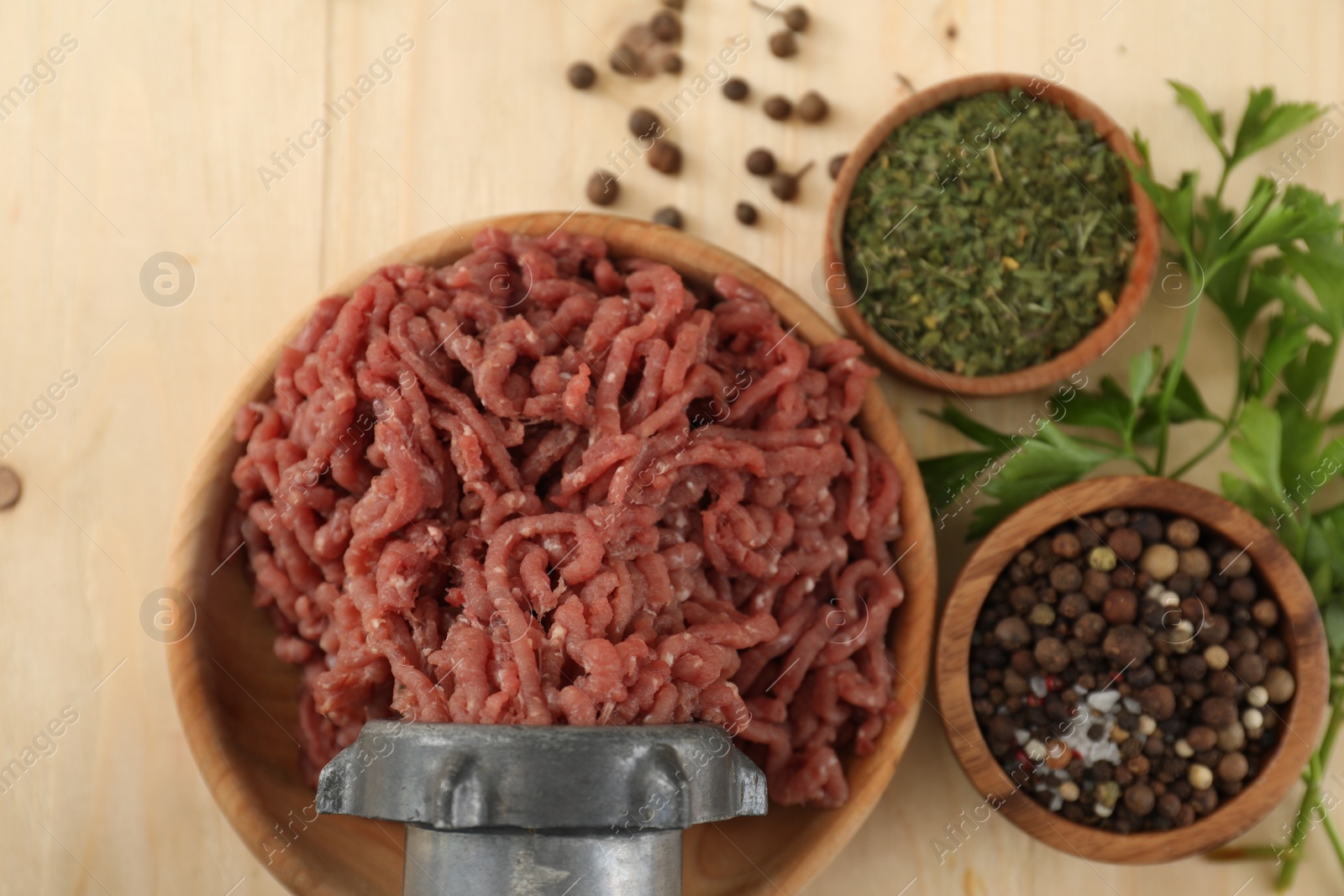 Photo of Mincing beef with meat grinder. Parsley and spices on wooden table, flat lay