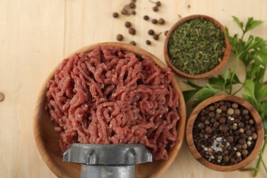 Mincing beef with meat grinder. Parsley and spices on wooden table, flat lay