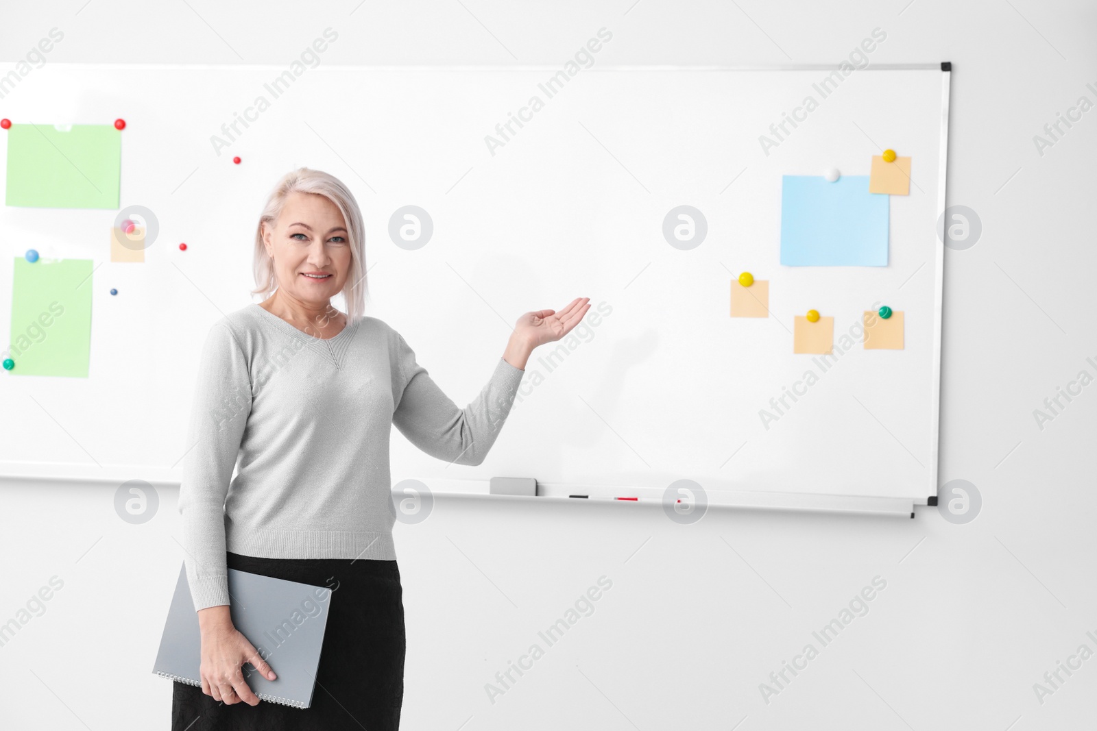 Photo of Mature teacher with notebook near whiteboard in classroom. Space for text