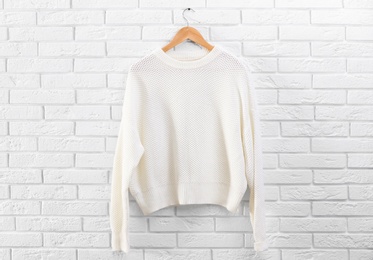 Hanger with stylish sweater on brick wall