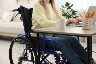 Photo of Woman in wheelchair using laptop at home, closeup
