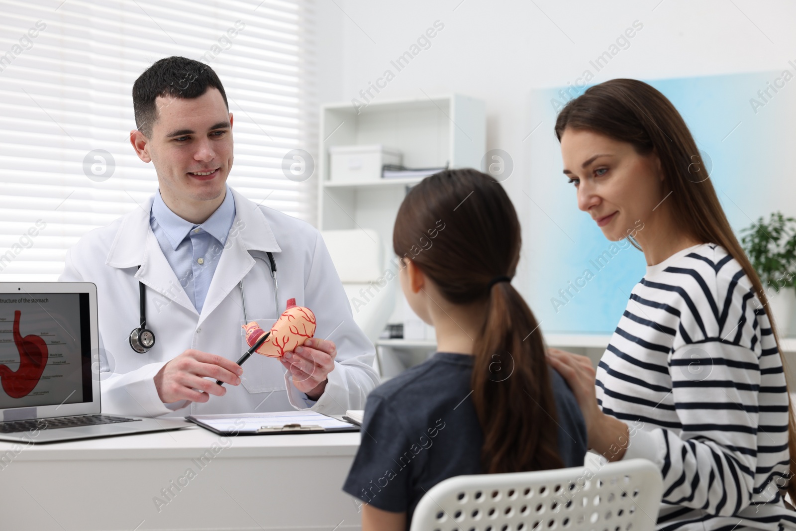Photo of Gastroenterologist with model of stomach consulting woman and her daughter in clinic