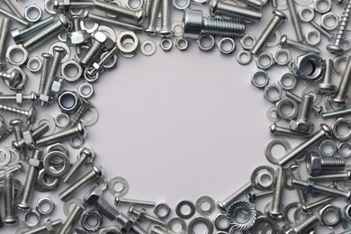 Frame of different metal bolts and nuts on white background, flat lay. Space for text