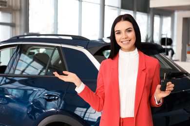 Photo of Saleswoman with key near car in dealership