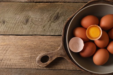 Bowl with raw chicken eggs on wooden table, top view. Space for text