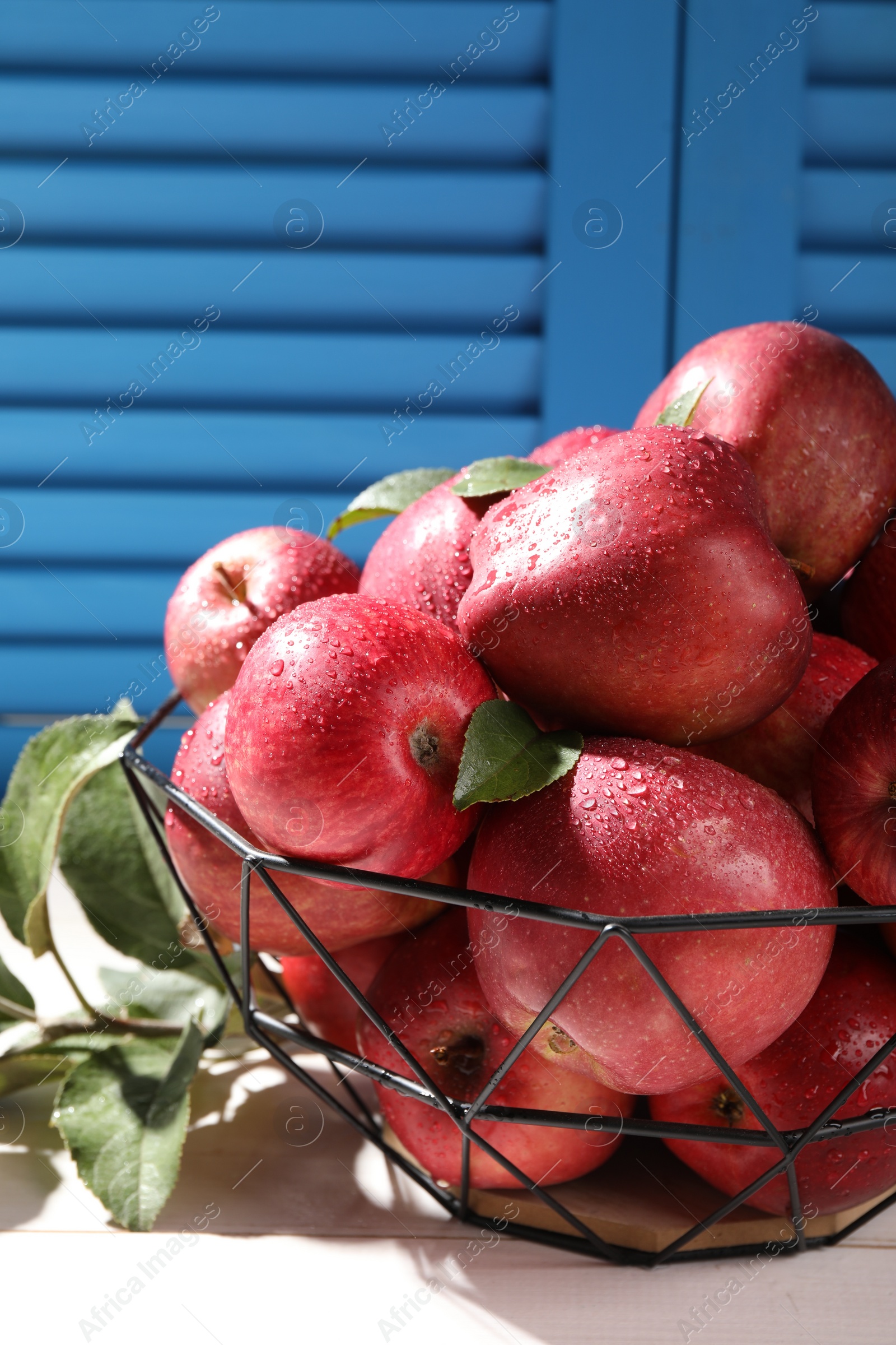 Photo of Metal bowl with wet red apples and green leaves on white table