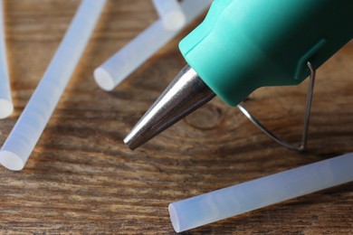 Photo of Hot glue gun and sticks on wooden table, closeup
