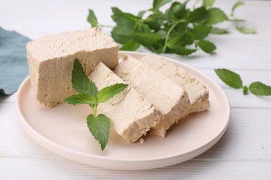 Plate with pieces of tasty halva and mint on white wooden table, closeup