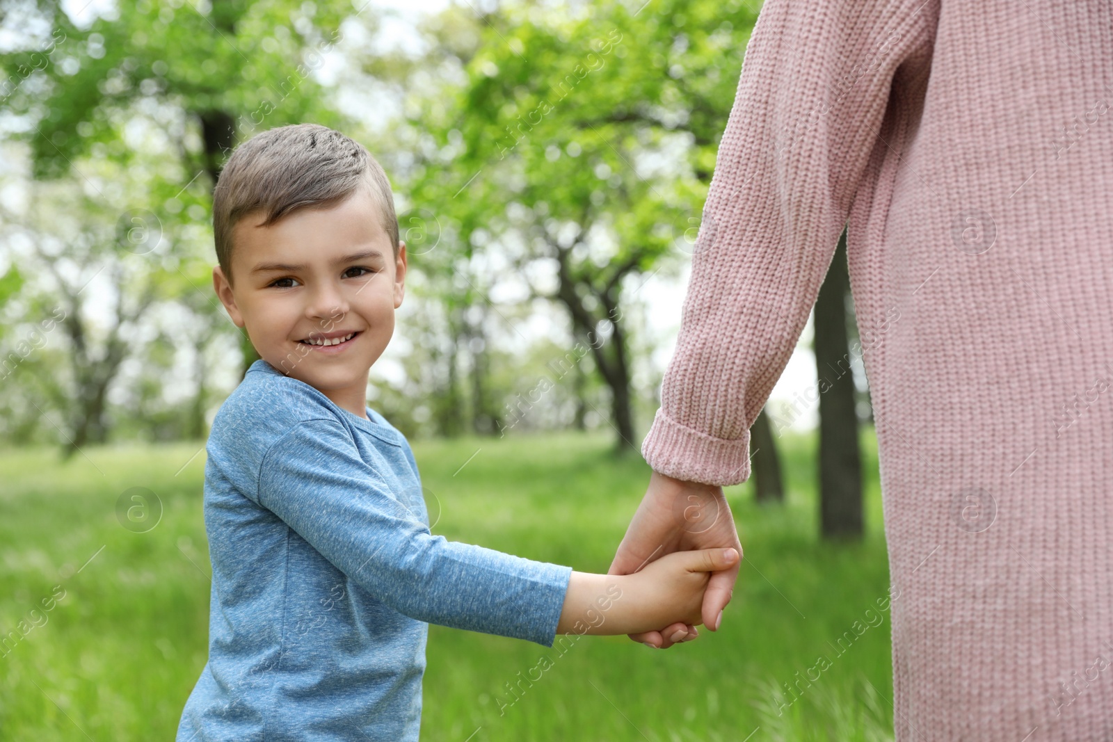 Photo of Happy little child holding hands with his mother in park. Family time