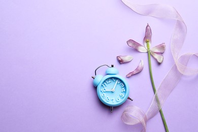 Beautiful tulip, ribbon and alarm clock on violet background, flat lay with space for text. Menopause concept