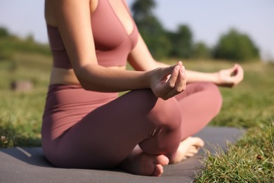Woman practicing yoga on mat outdoors, closeup. Lotus pose