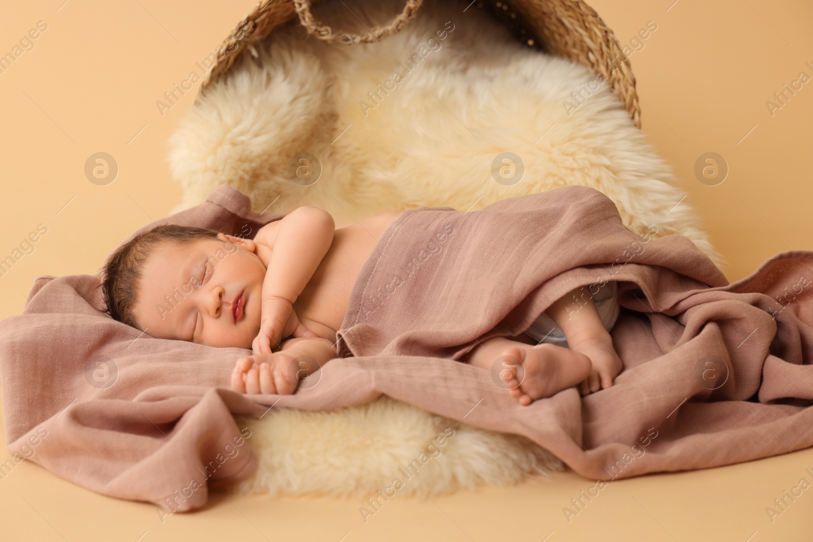 Photo of Adorable newborn baby sleeping on faux fur near overturned wicker basket against beige background